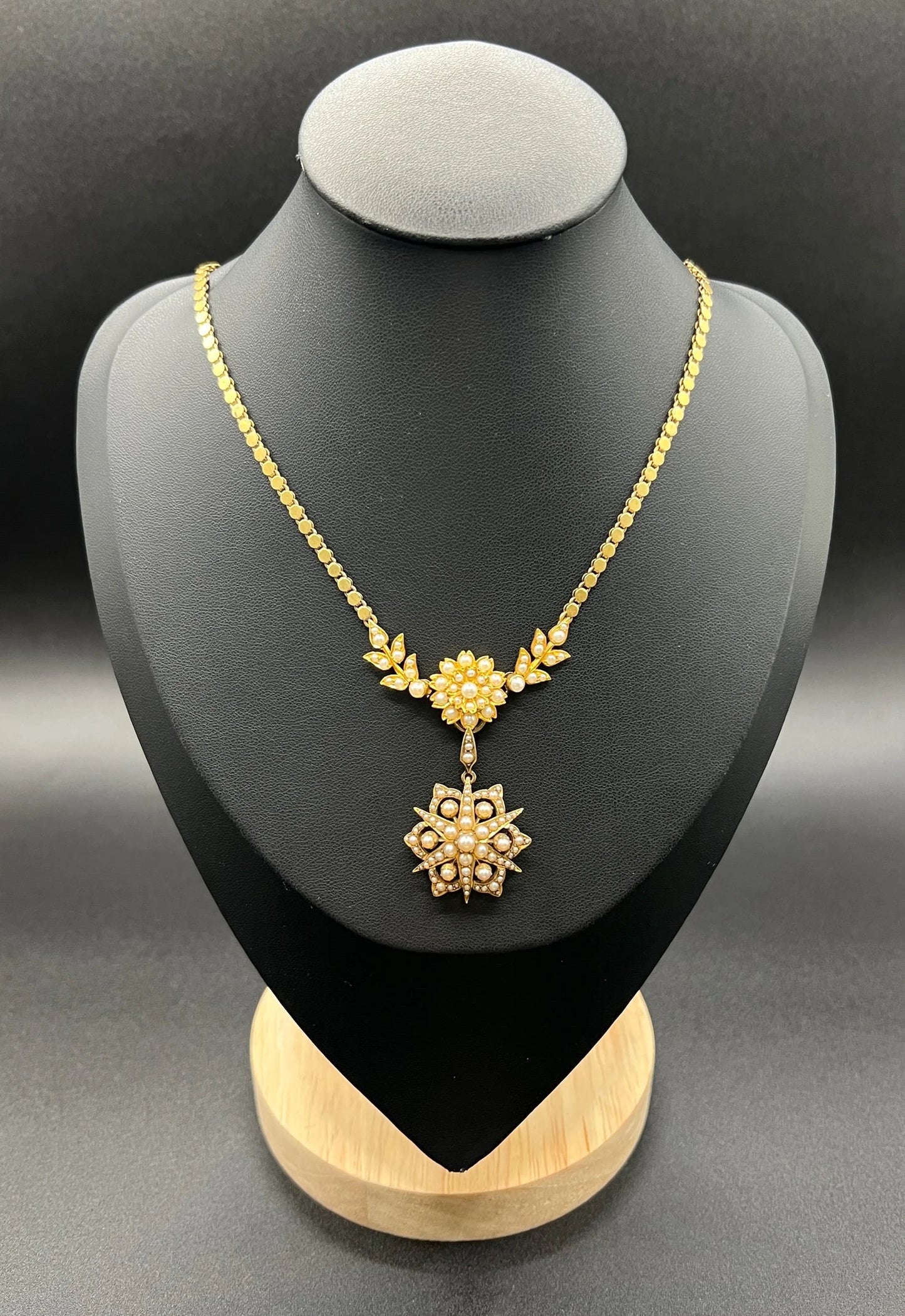 A yellow gold pearl floral necklace with integrated chain, on a black jewellery bust