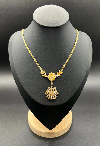 A yellow gold pearl floral necklace with integrated chain, on a black jewellery bust