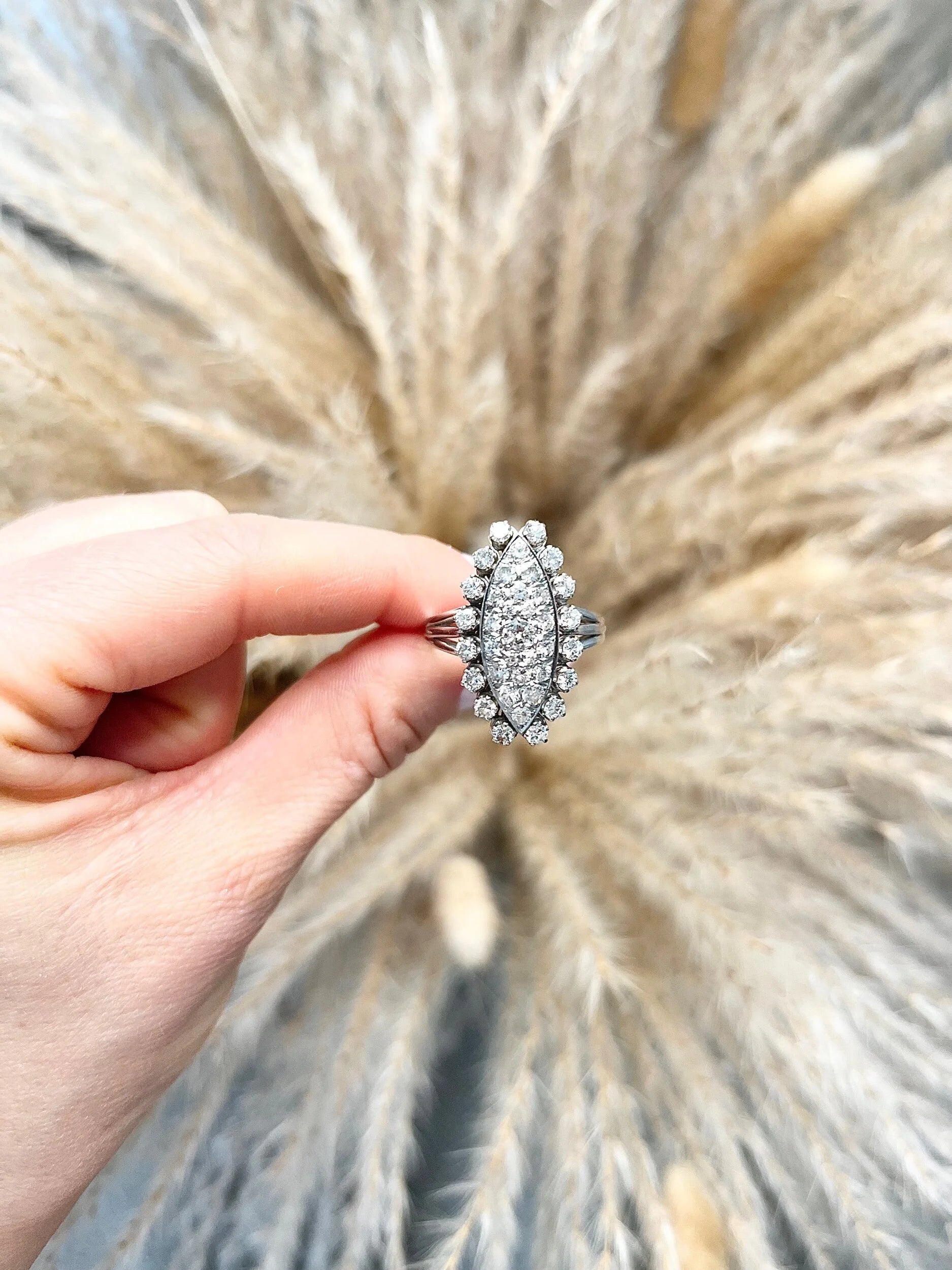 A navette shaped diamond cluster ring in white metal, held in a hand