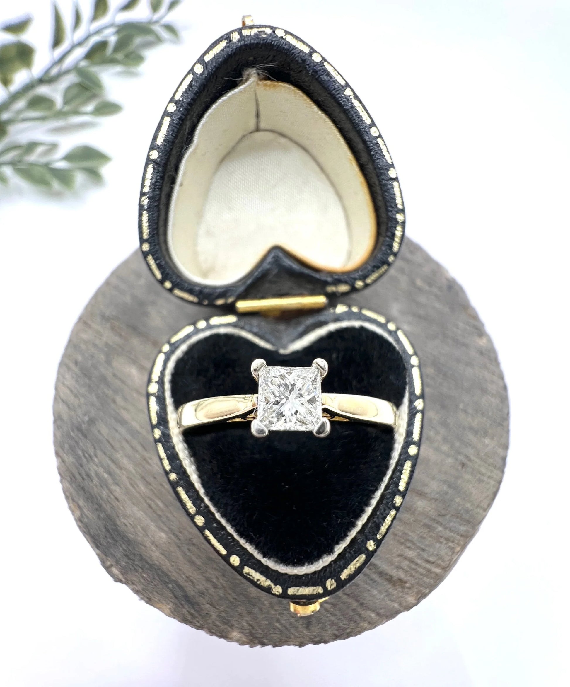 A solitaire princess cut diamond ring in yellow and white gold, in a heart-shaped ring box