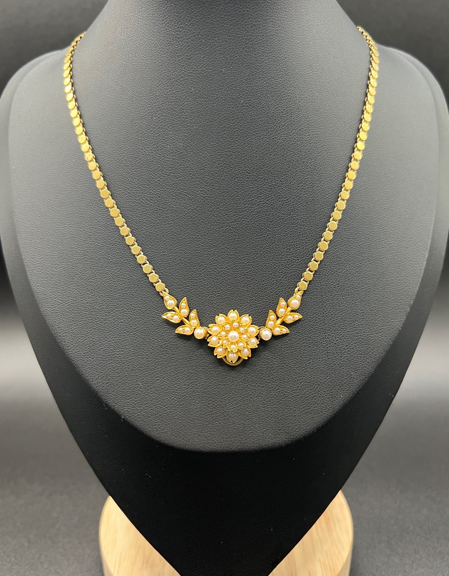 A yellow gold pearl floral necklace with integrated chain, on a black jewellery bust