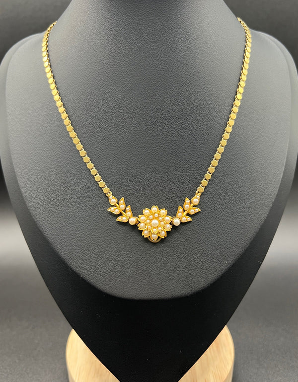 A yellow gold pearl floral necklace with integrated chain, on a black jewellery bust