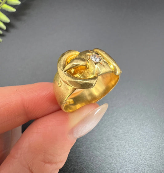 A yellow gold diamond set buckle ring, held in a hand