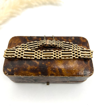 A yellow gold gate bracelet, laid on an antique box