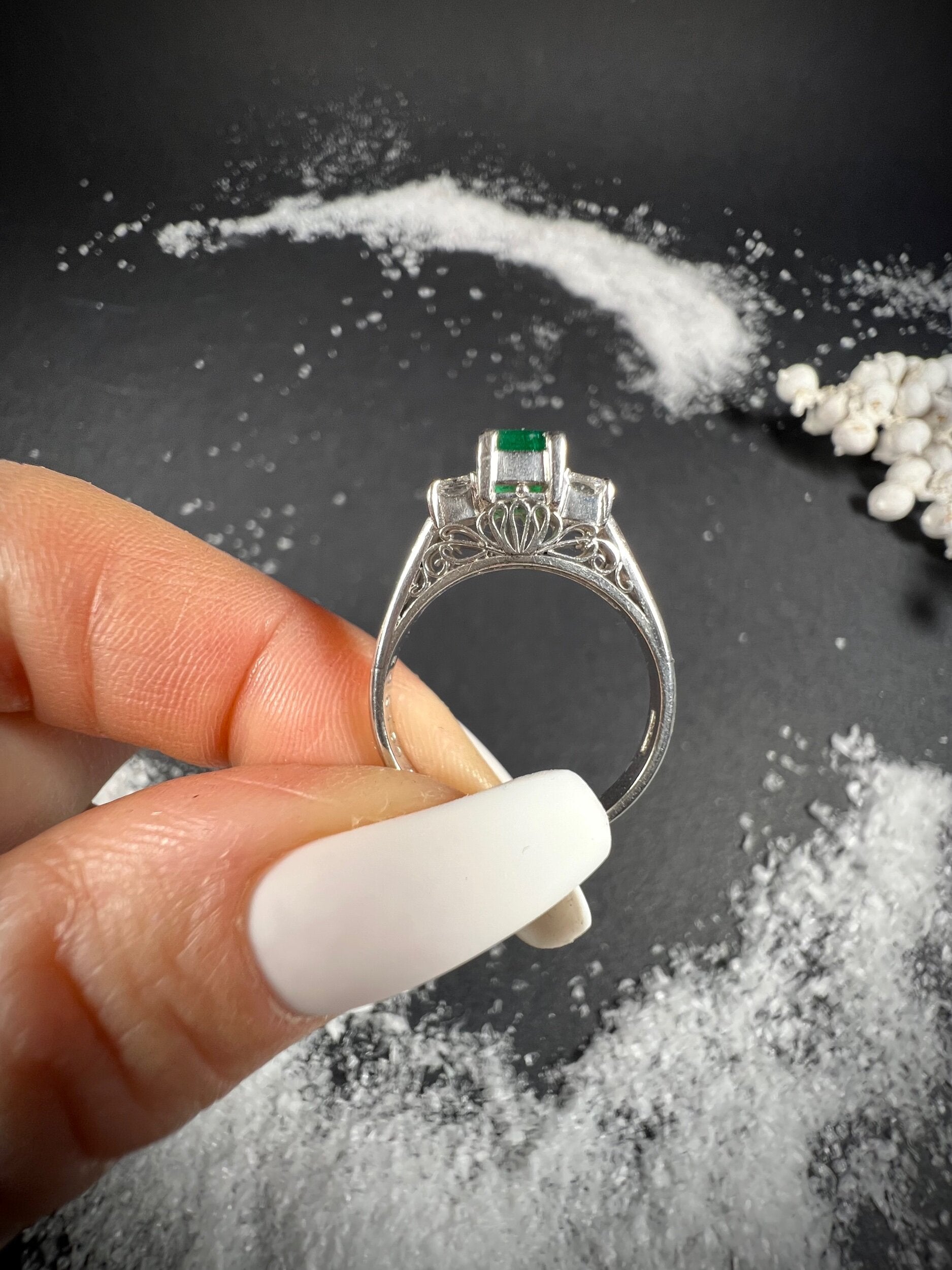 A three stone emerald and diamond ring in platinum, held in a hand