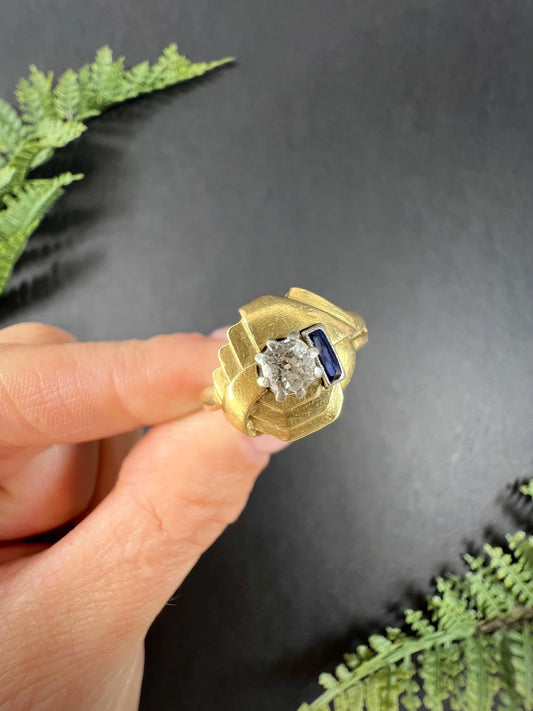 A yellow gold diamond and sapphire cocktail ring, held in a hand