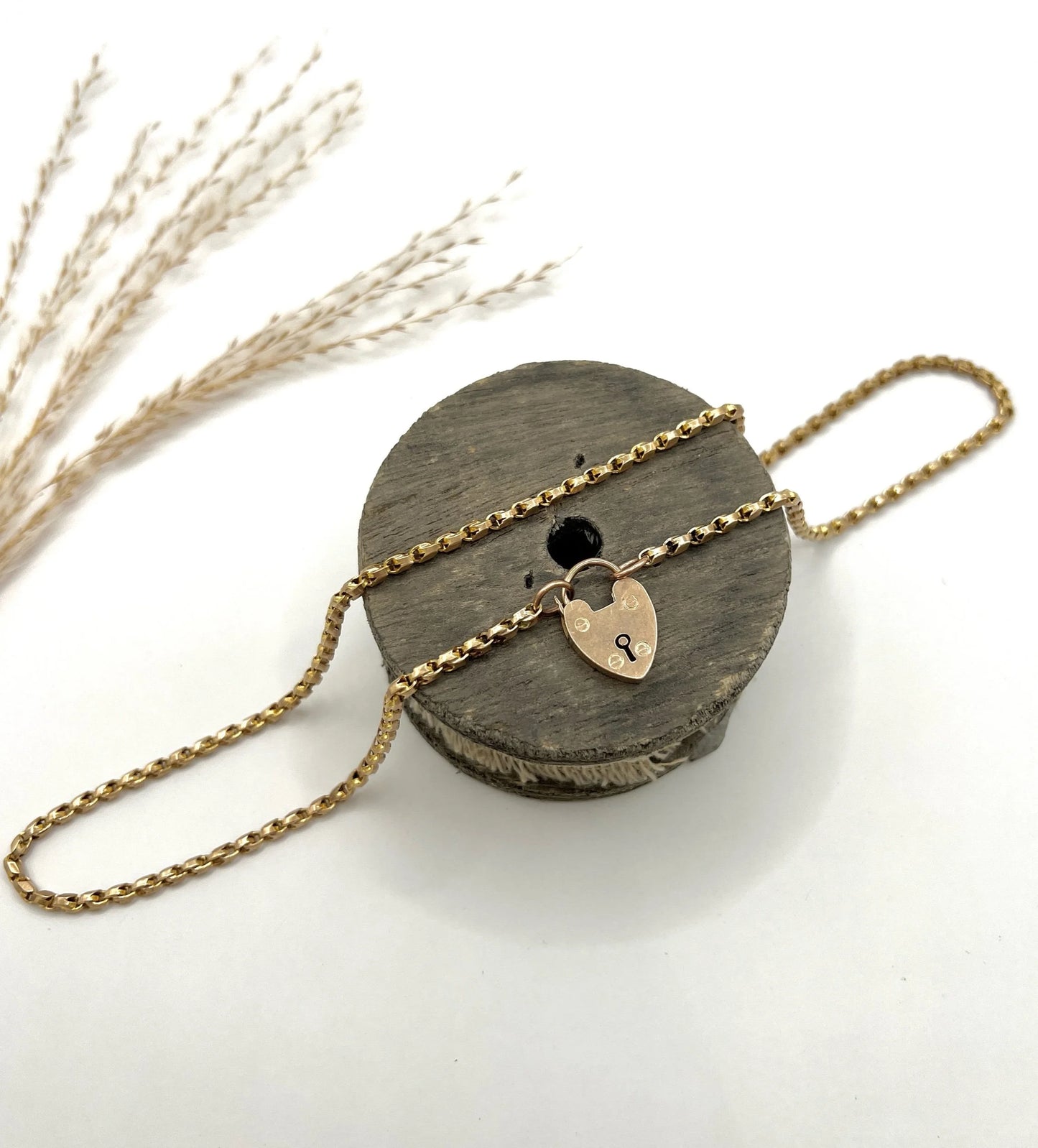 A gold chain necklace with gold heart padlock, on a wooden spool