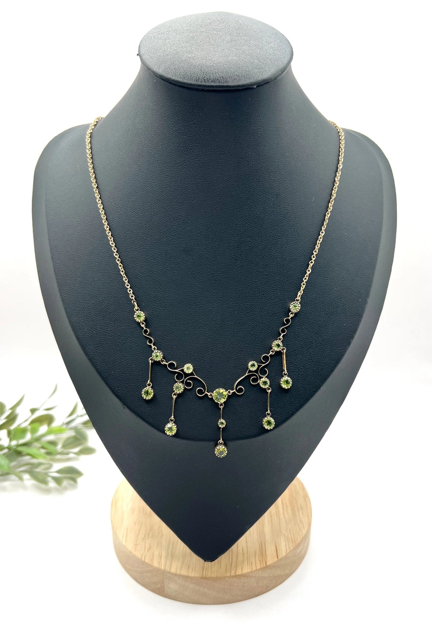 A yellow gold swag necklace with peridot drops, on a black jewellery bust