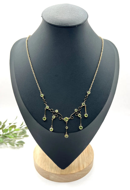 A yellow gold swag necklace with peridot drops, on a black jewellery bust