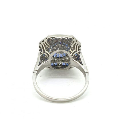 Diamond and Calibre Sapphire Target Cluster Dress Ring in Platinum; central diamond within a calibre sapphire halo, surrounded by brilliant-cut diamonds and a further outer border of sapphires, with diamond and sapphire set shoulders and a beautifully pierced under-gallery