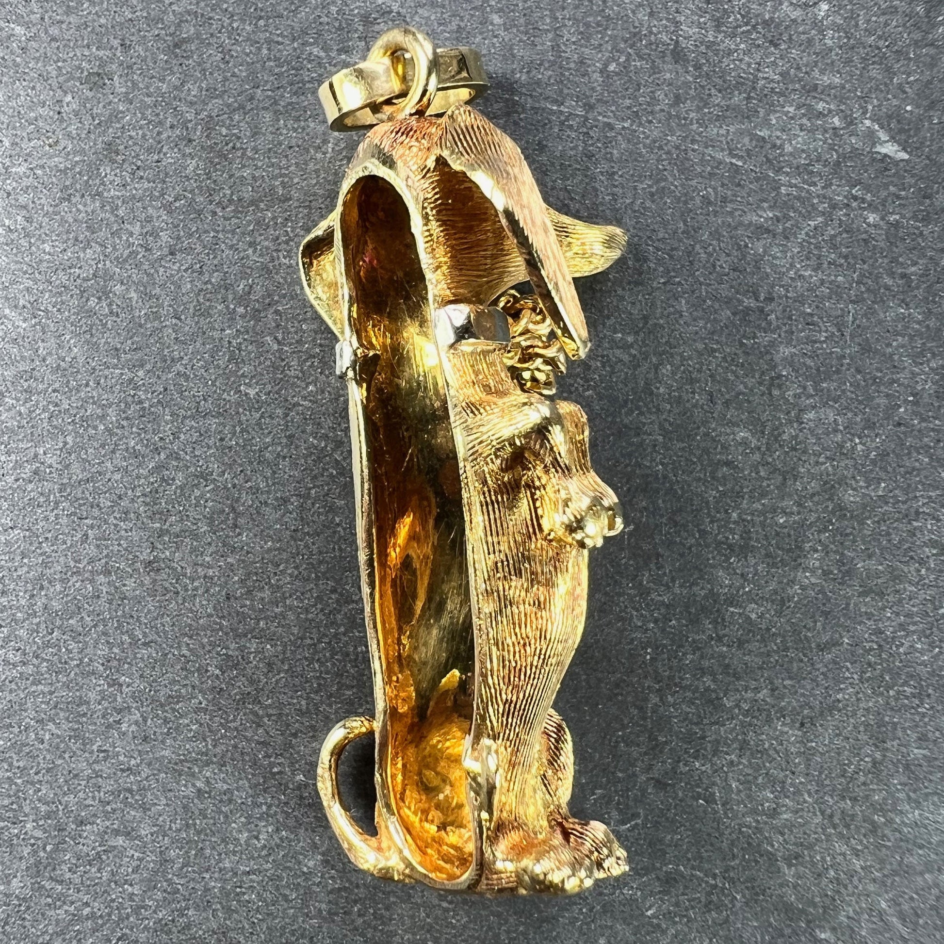 A yellow gold dachshund dog charm with ruby eyes, on a dark background