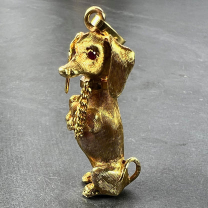 A yellow gold dachshund dog charm with ruby eyes, on a grey background