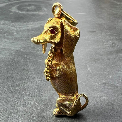 A yellow gold dachshund dog charm with ruby eyes, on a grey background