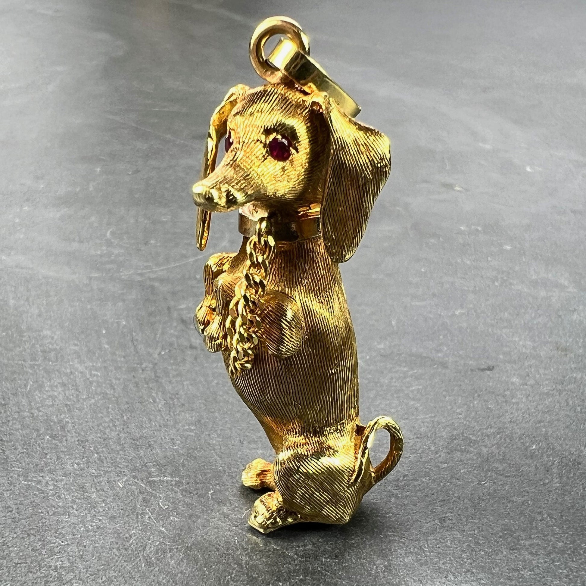 A yellow gold dachshund dog charm with ruby eyes, on a grey background