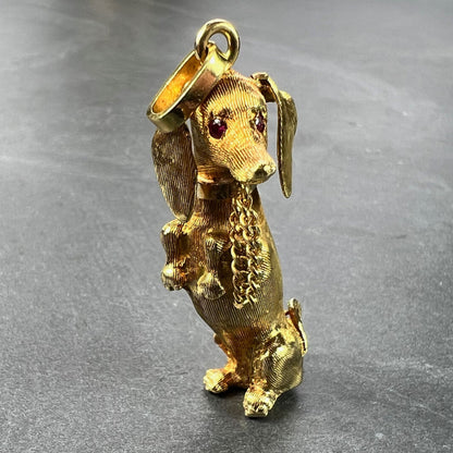 A yellow gold dachshund dog charm with ruby eyes, on a grey background