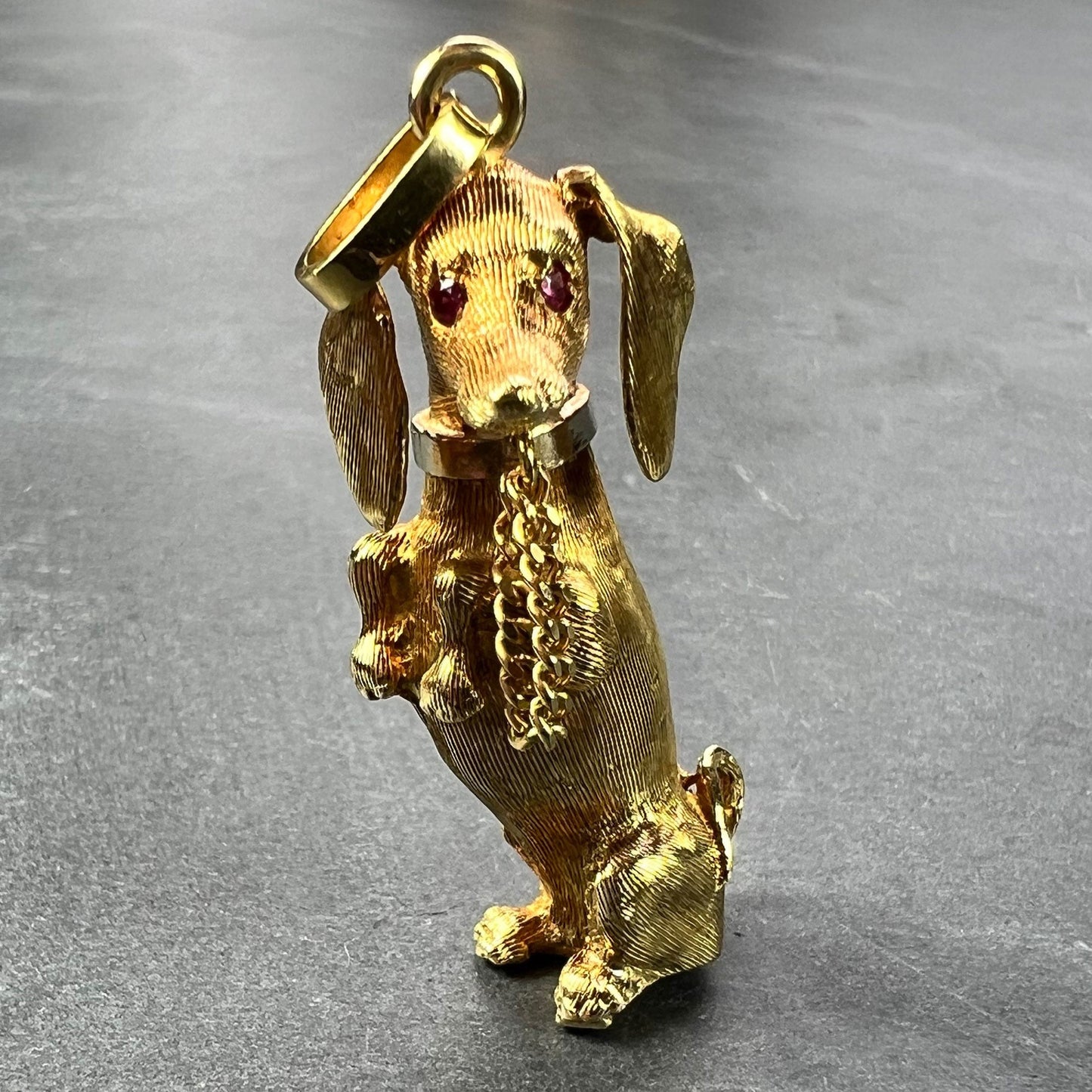 A yellow gold dachshund dog charm with ruby eyes, on a grey background