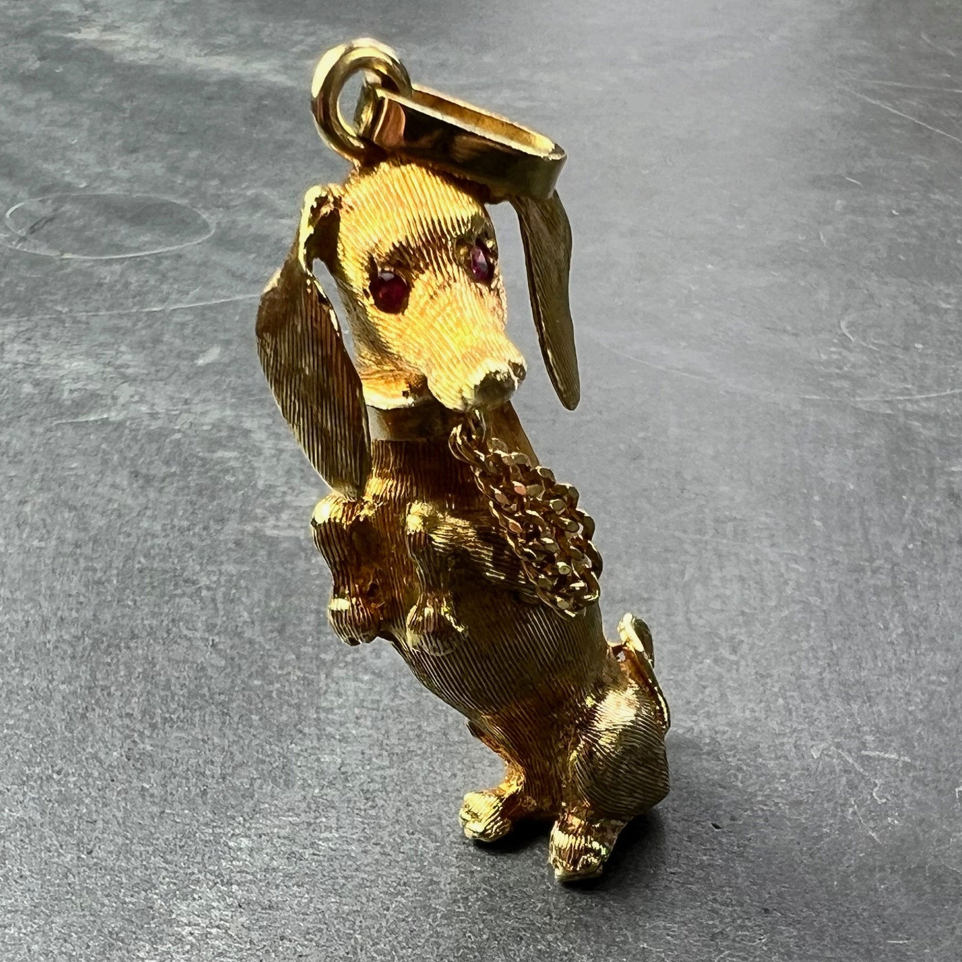 A yellow gold dachshund dog charm with ruby eyes, on a grey background