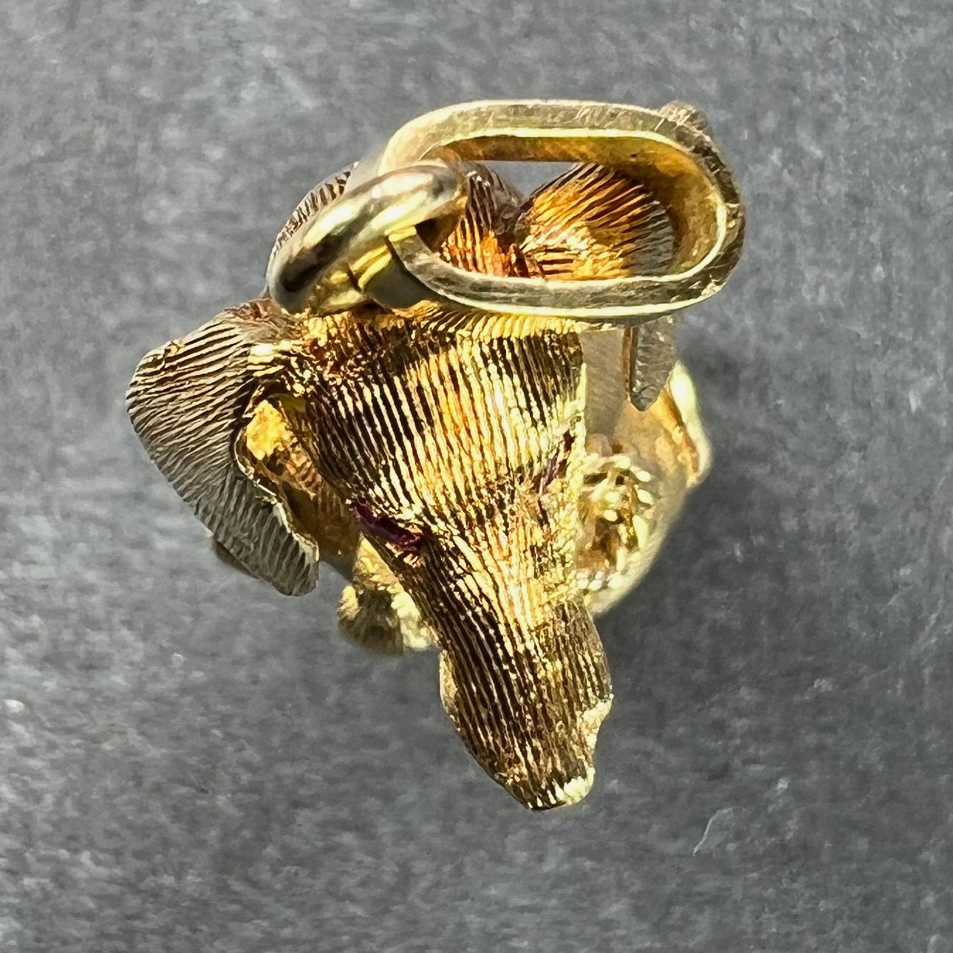 A yellow gold dachshund dog charm with ruby eyes, on a grey background