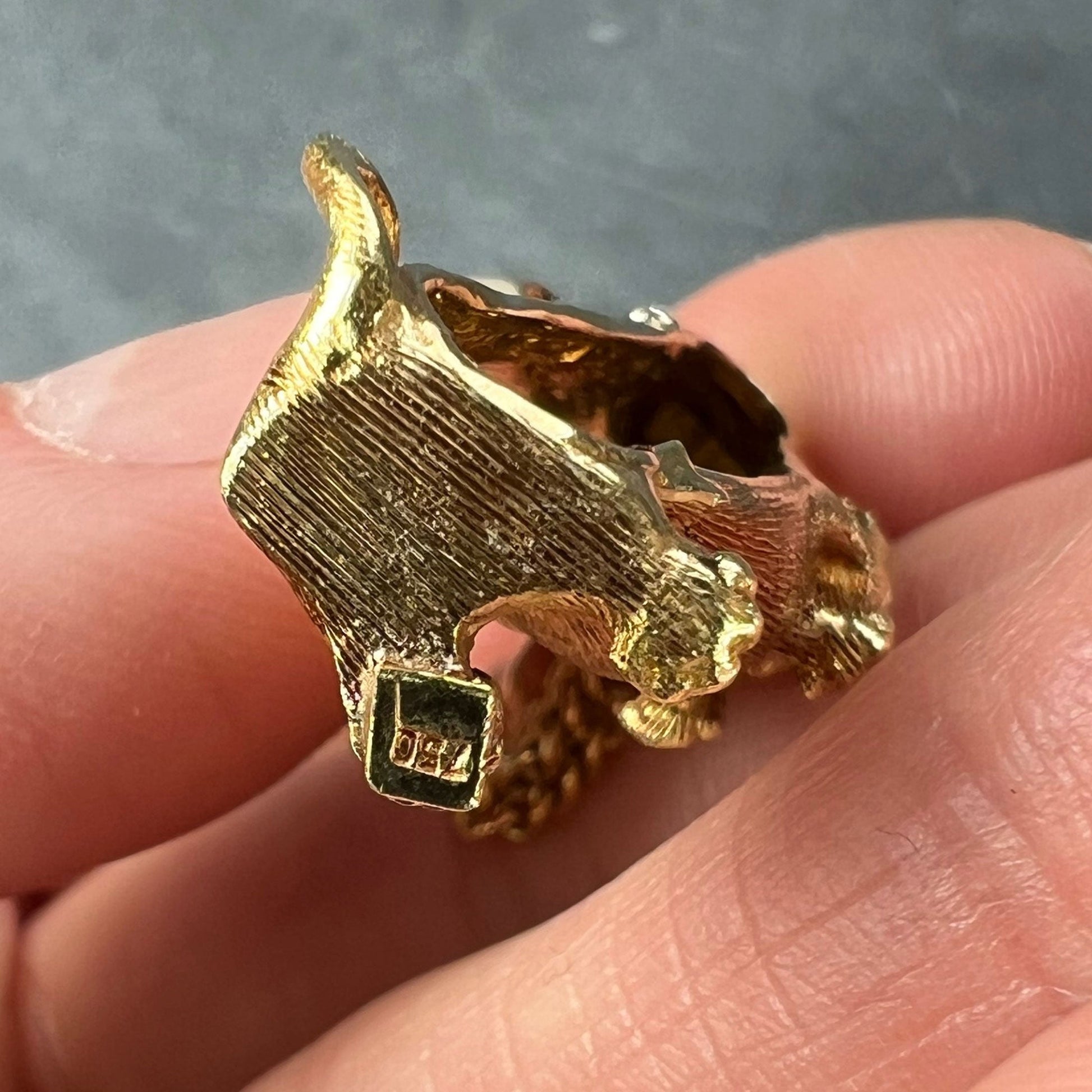 A yellow gold dachshund dog charm with ruby eyes, stamped 750, held in a hand, on a grey background