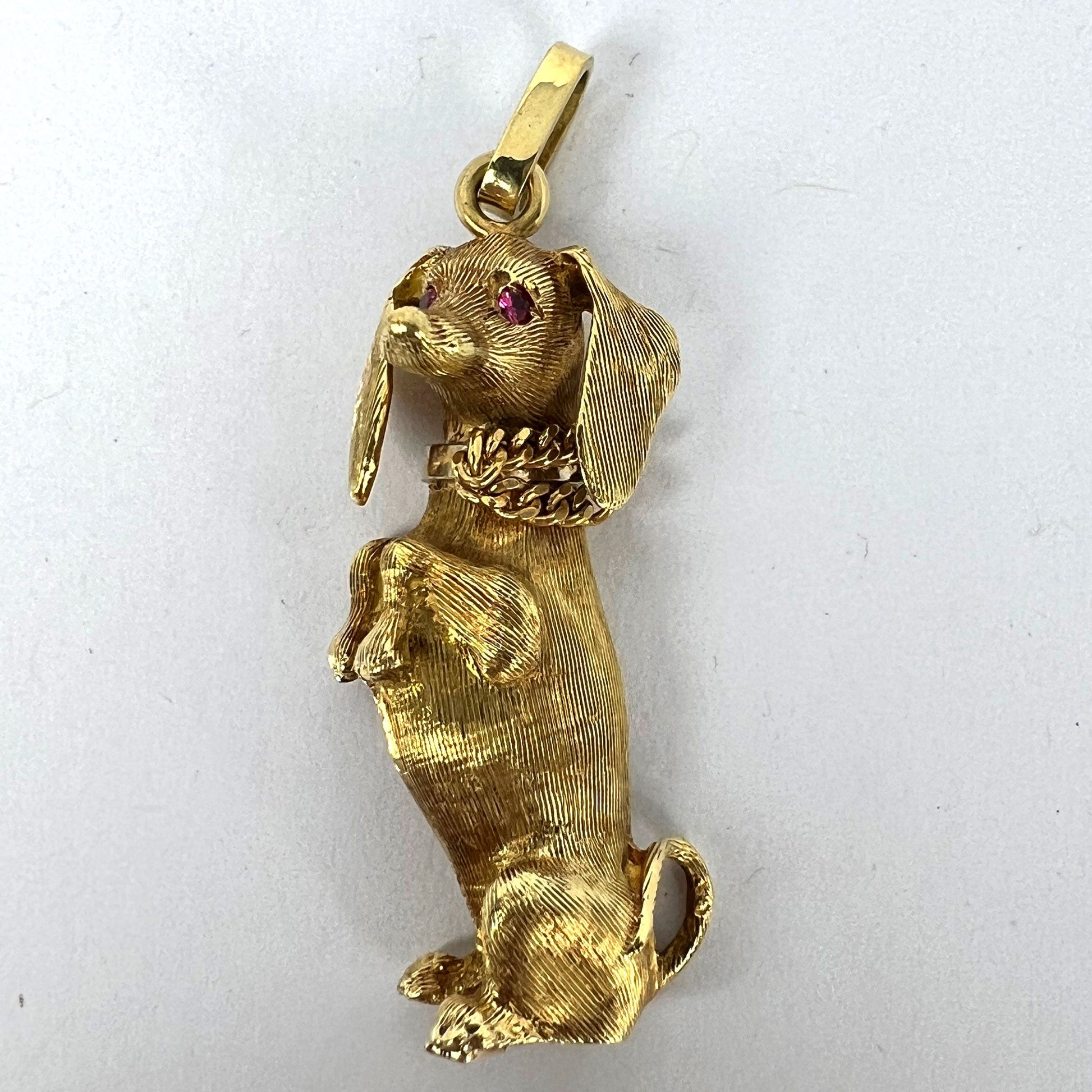 A yellow gold dachshund dog charm with ruby eyes, on a white background