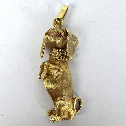 A yellow gold dachshund dog charm with ruby eyes, on a white background