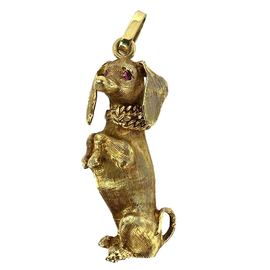 A yellow gold dachshund dog charm with ruby eyes, on a white background