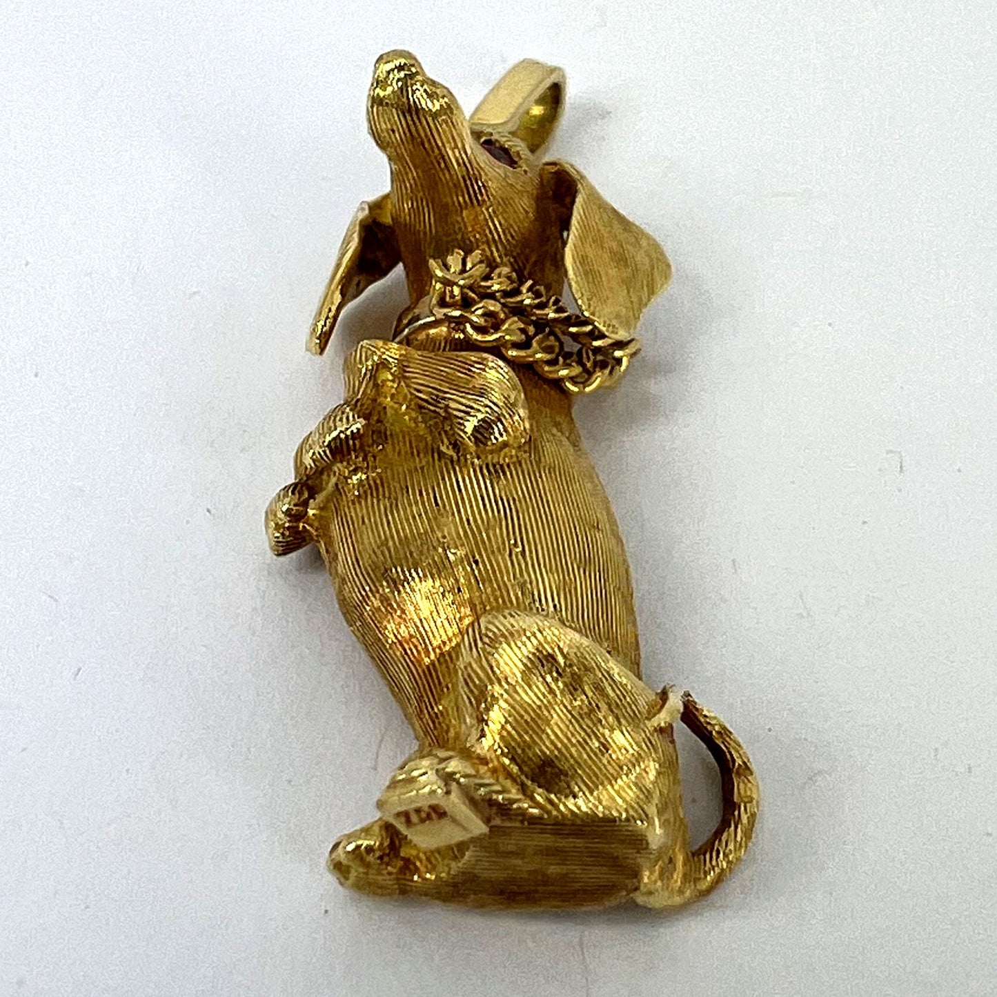 A yellow gold dachshund dog charm with ruby eyes, on a white background