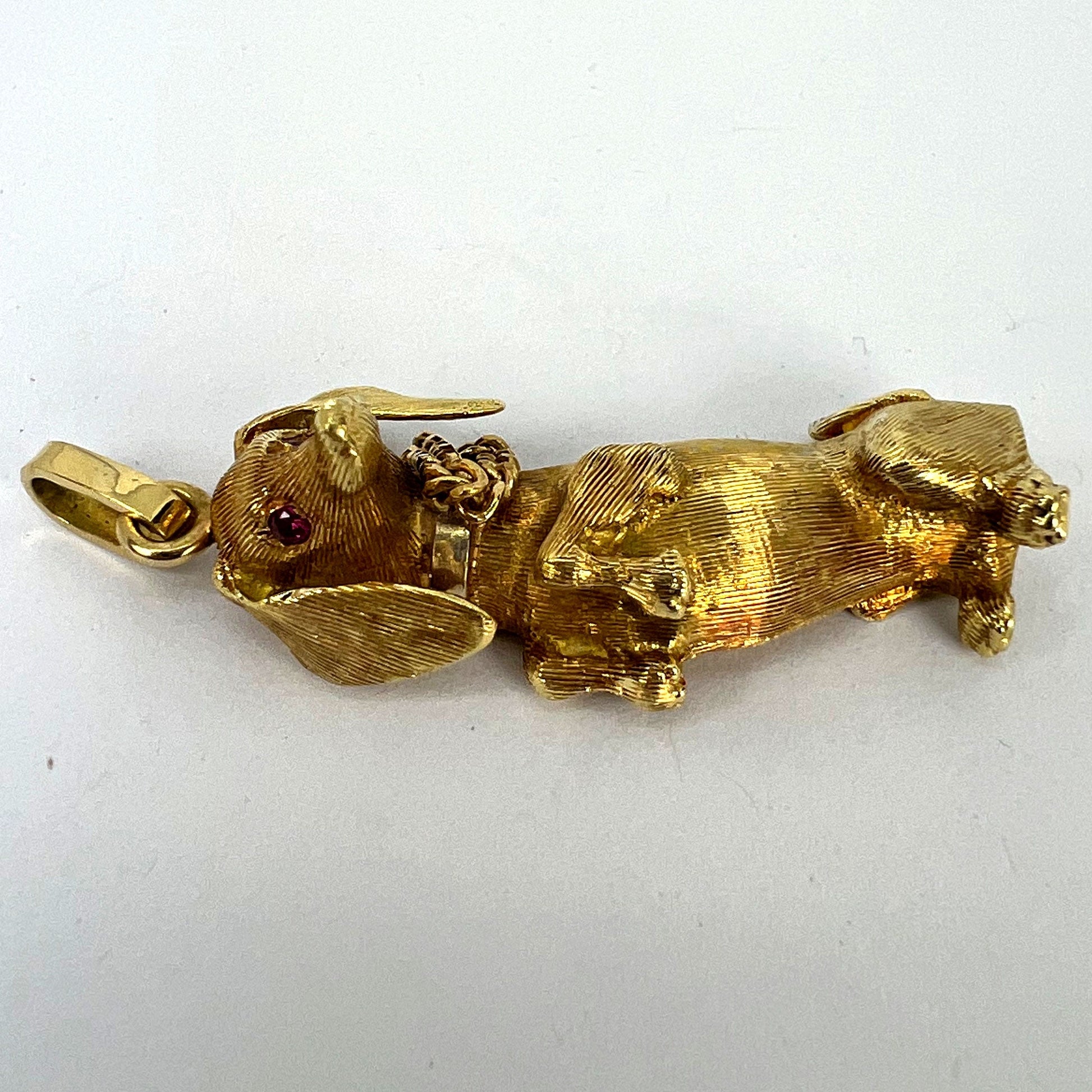 A yellow gold dachshund dog charm with ruby eyes, on a white background
