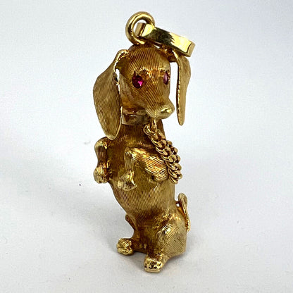 A yellow gold dachshund dog charm with ruby eyes, on a white background