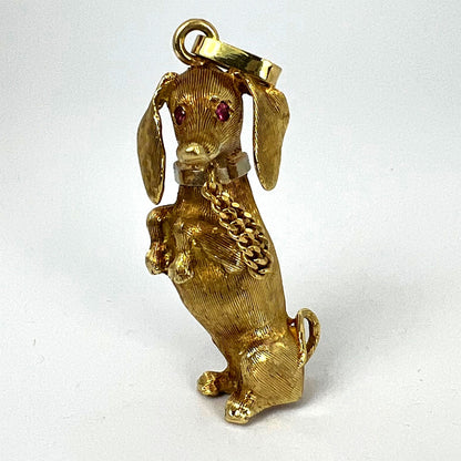 A yellow gold dachshund dog charm with ruby eyes, on a white background