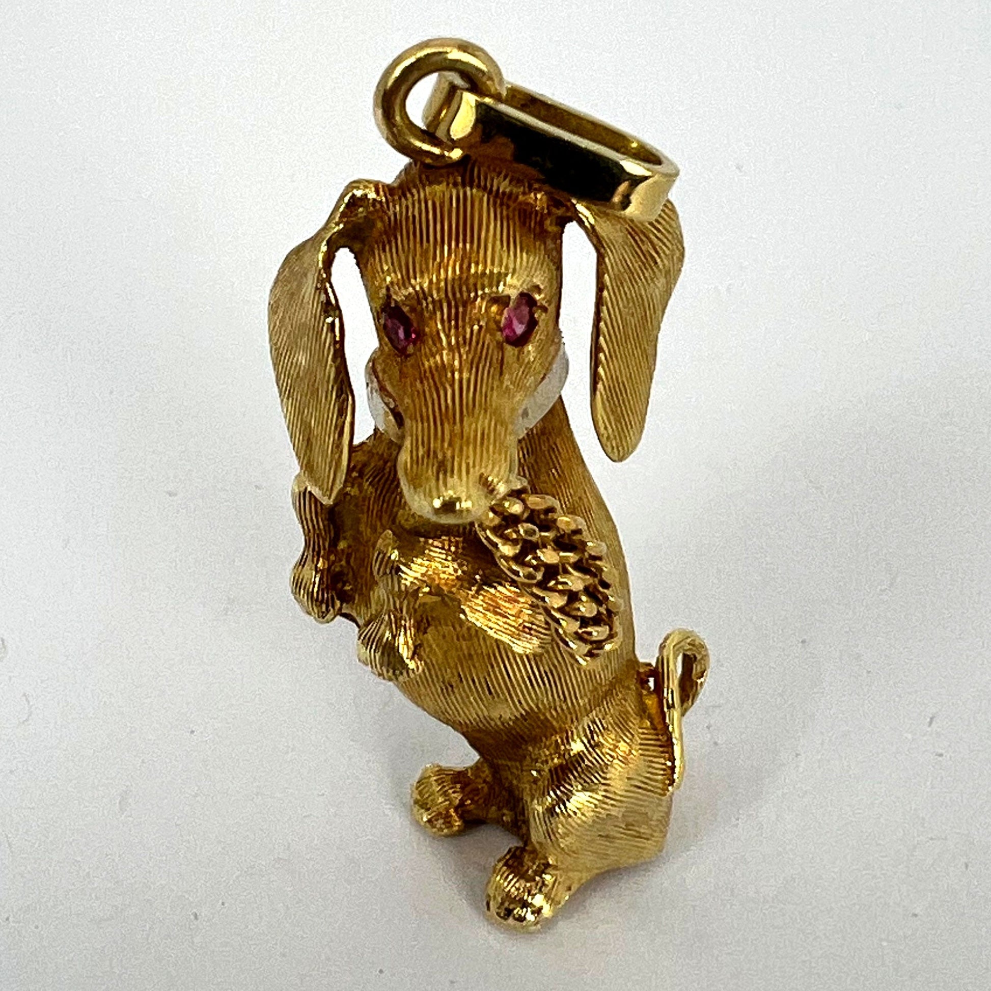 A yellow gold dachshund dog charm with ruby eyes, on a white background