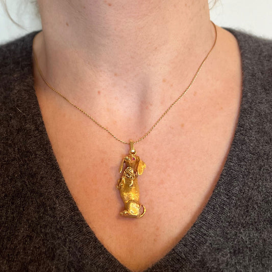 A yellow gold dachshund dog charm with ruby eyes, modelled on a gold chain