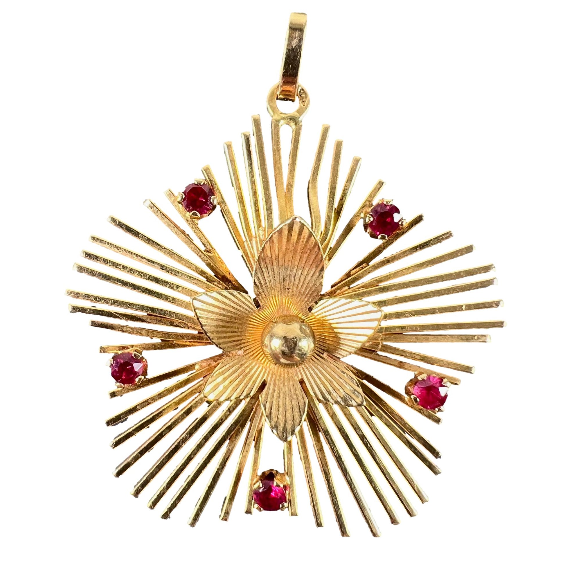 A yellow gold floral sunburst pendant with rubies, on a white background