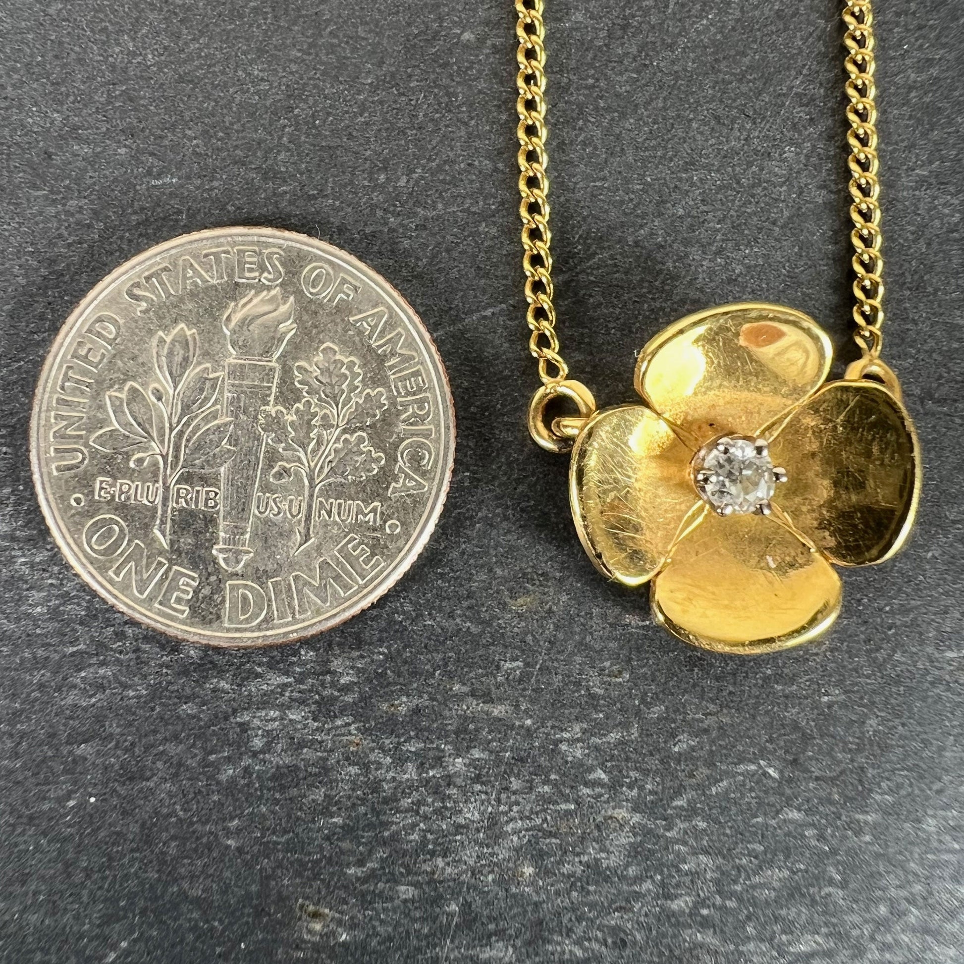 A yellow gold and diamond flower pendant necklace, next to a dime coin on a grey background