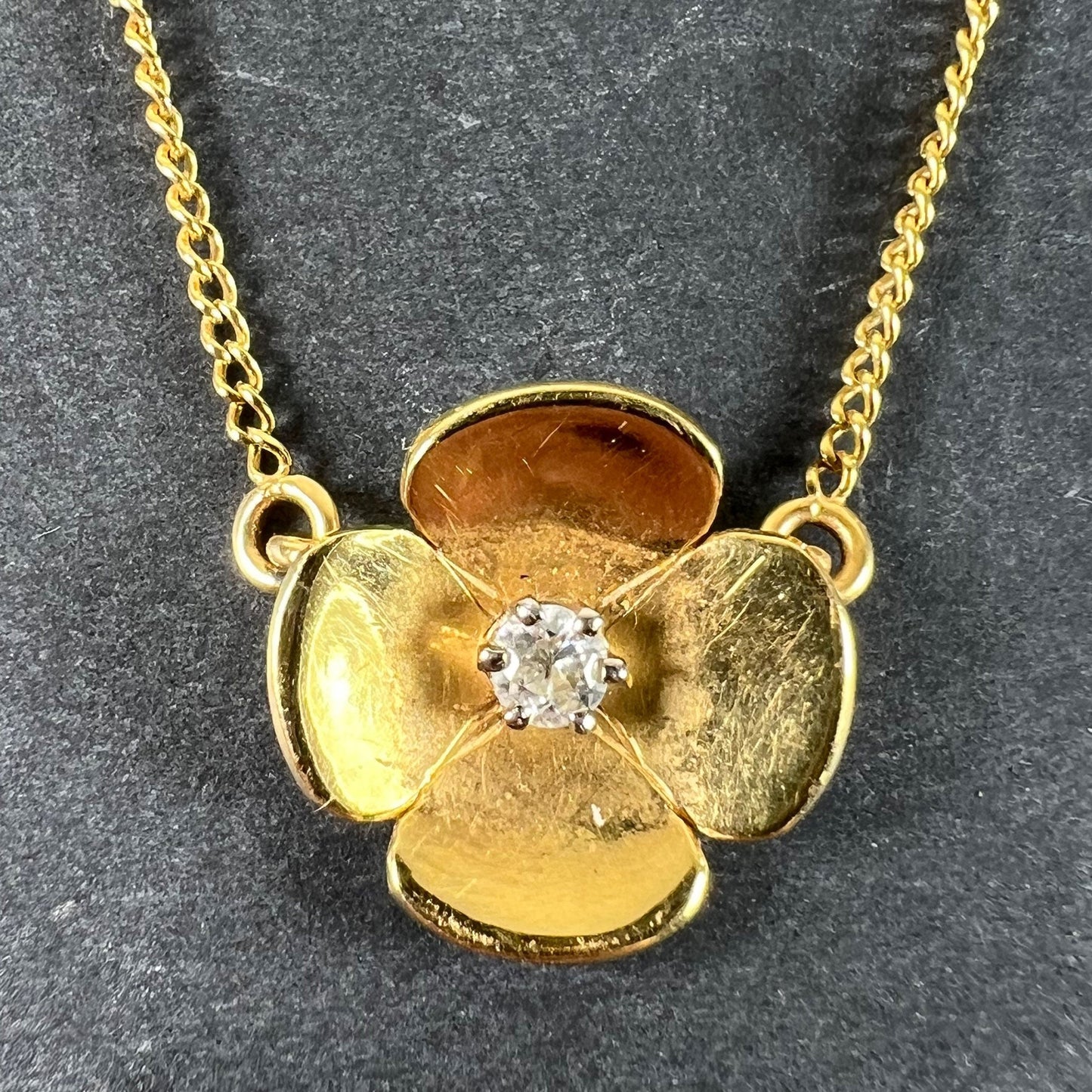 A yellow gold and diamond flower pendant necklace, on a grey background