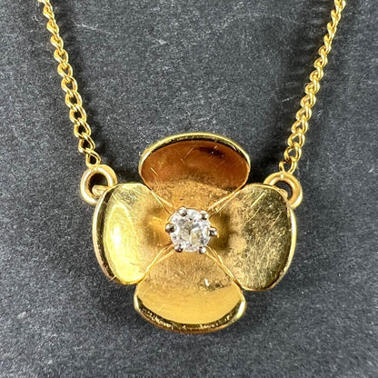 A yellow gold and diamond flower pendant necklace, on a grey background
