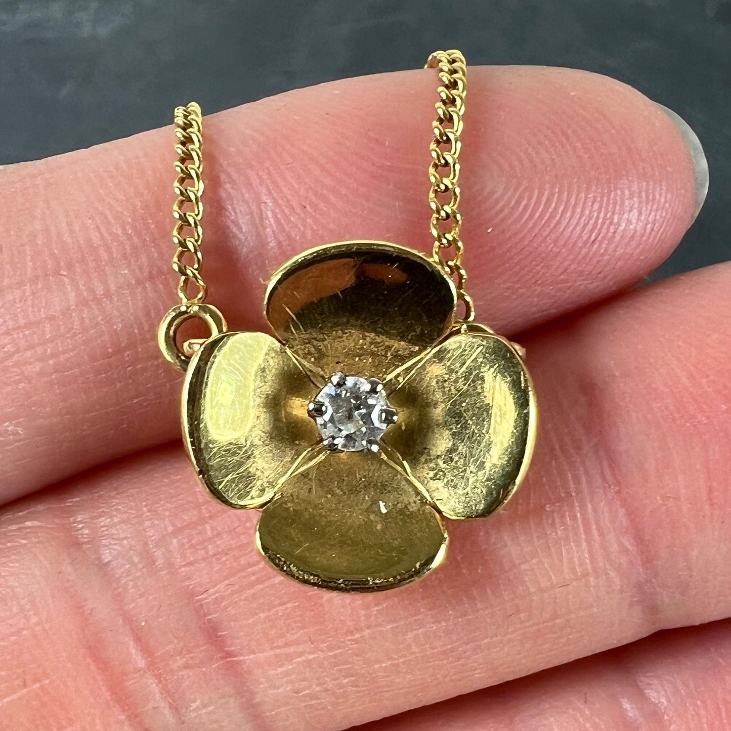 A yellow gold and diamond flower pendant necklace, held by a hand on a grey background