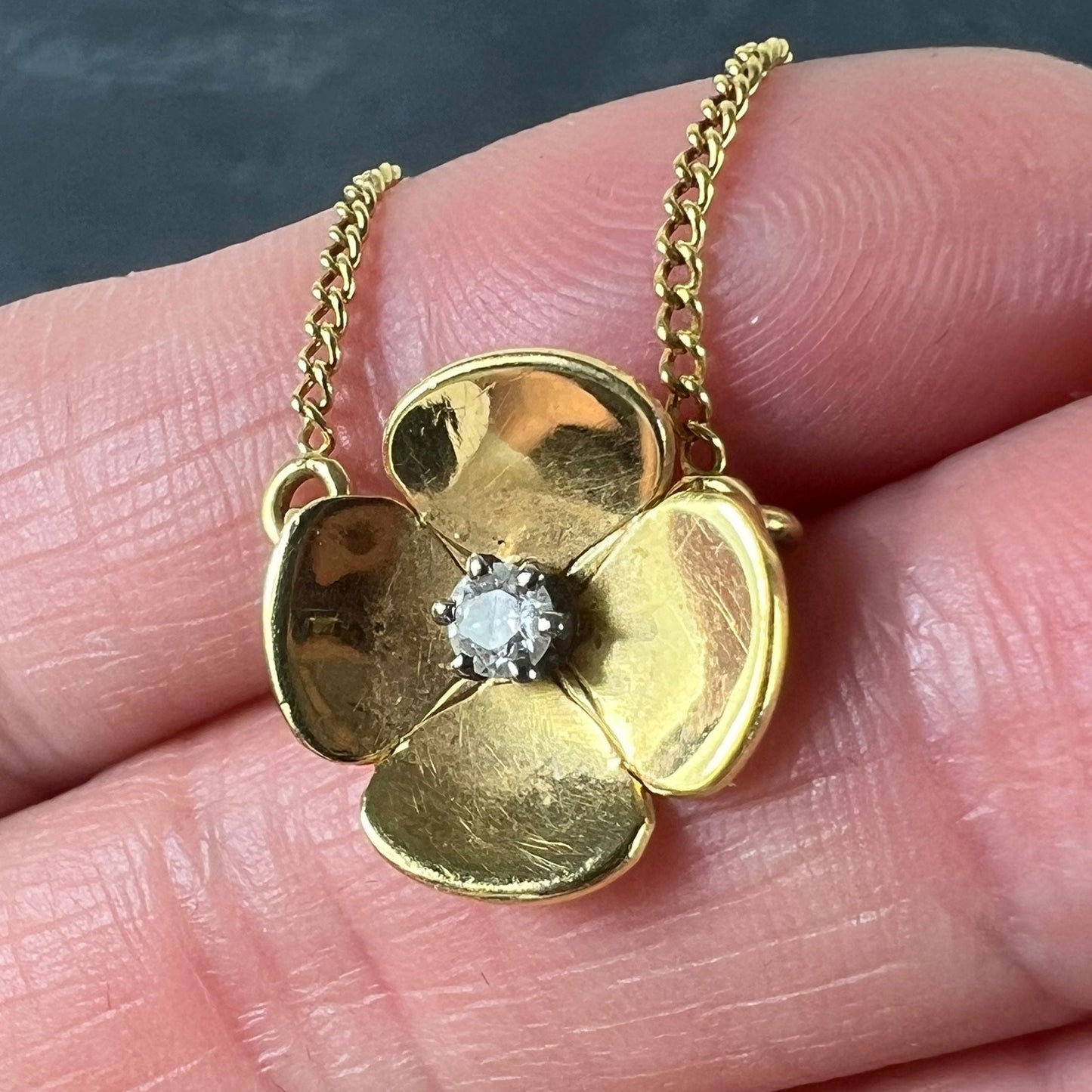 A yellow gold and diamond flower pendant necklace, held in a hand on a grey background