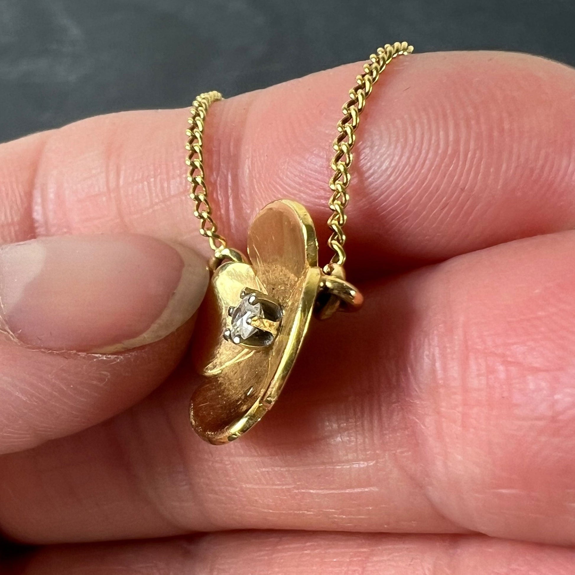 A yellow gold and diamond flower pendant necklace, held in a hand on a grey background
