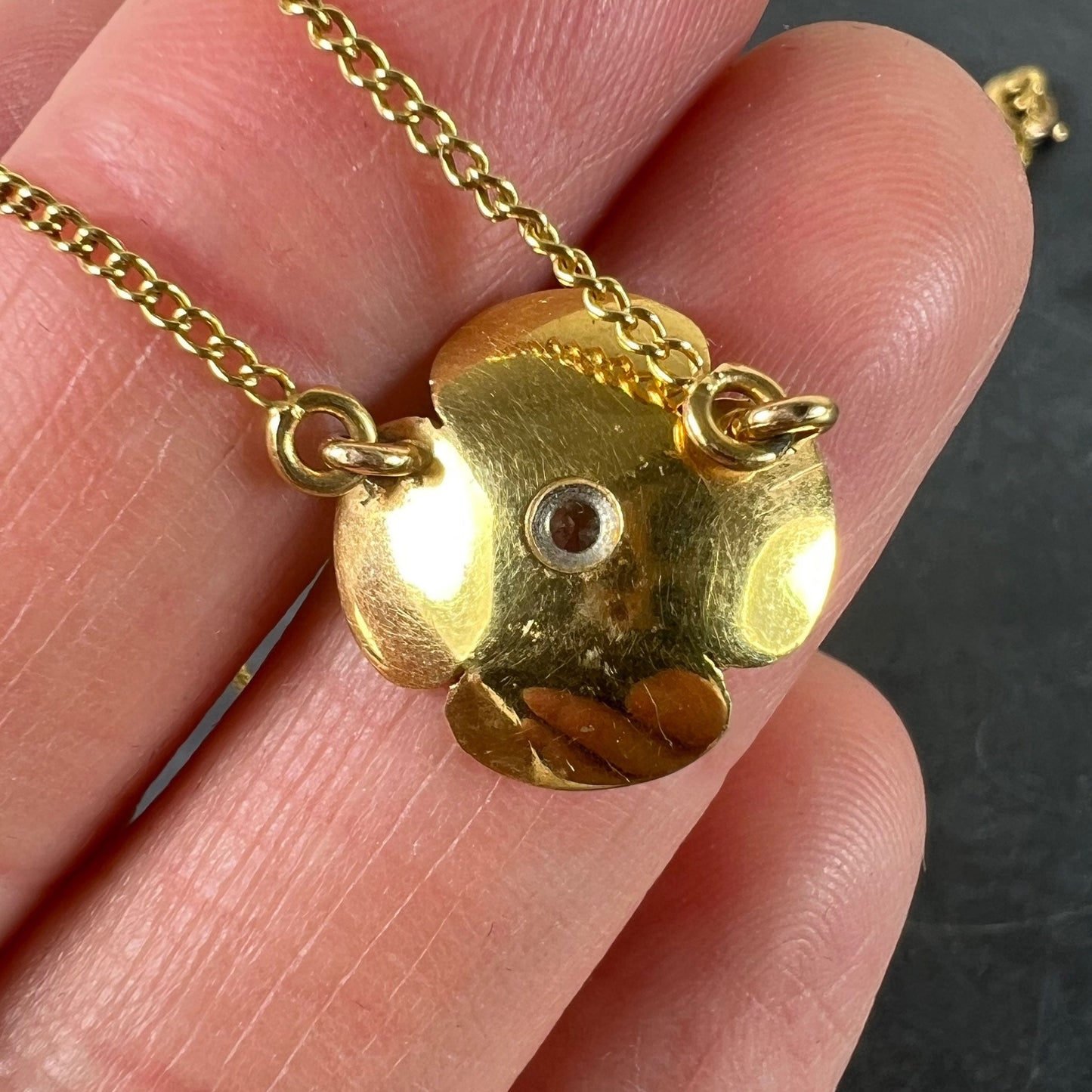 A yellow gold and diamond flower pendant necklace, held in a hand on a grey background