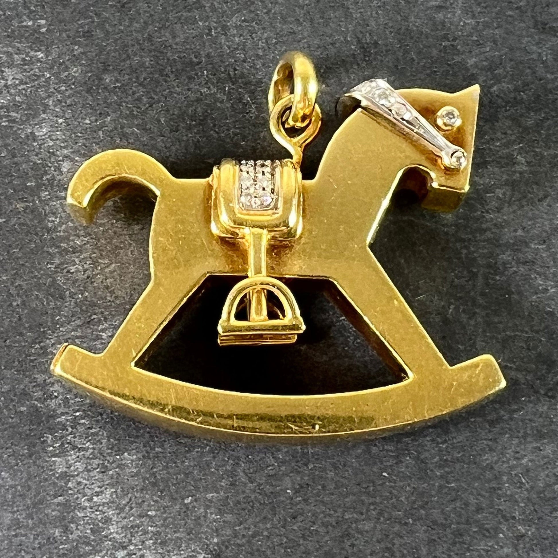 A yellow and white gold rockinghorse pendant with diamonds, on a grey background