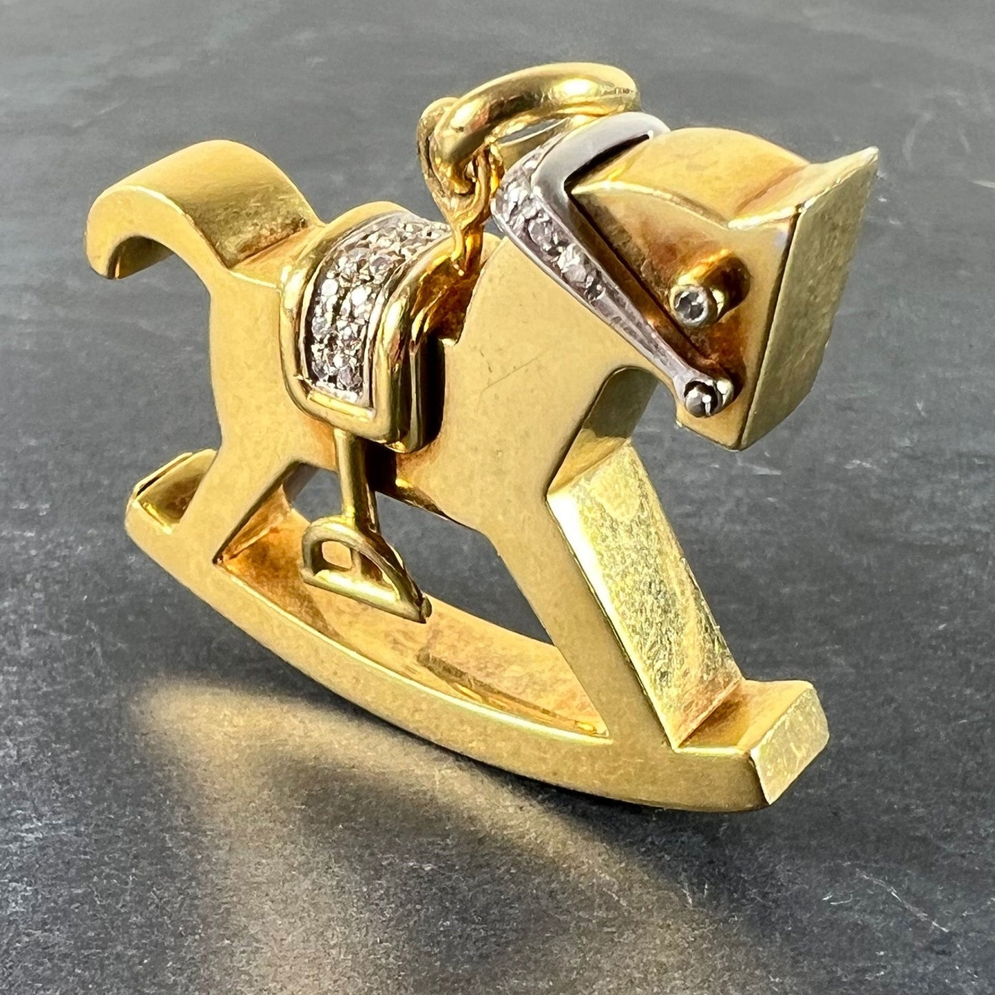 A yellow and white gold rockinghorse pendant with diamonds, on a grey background