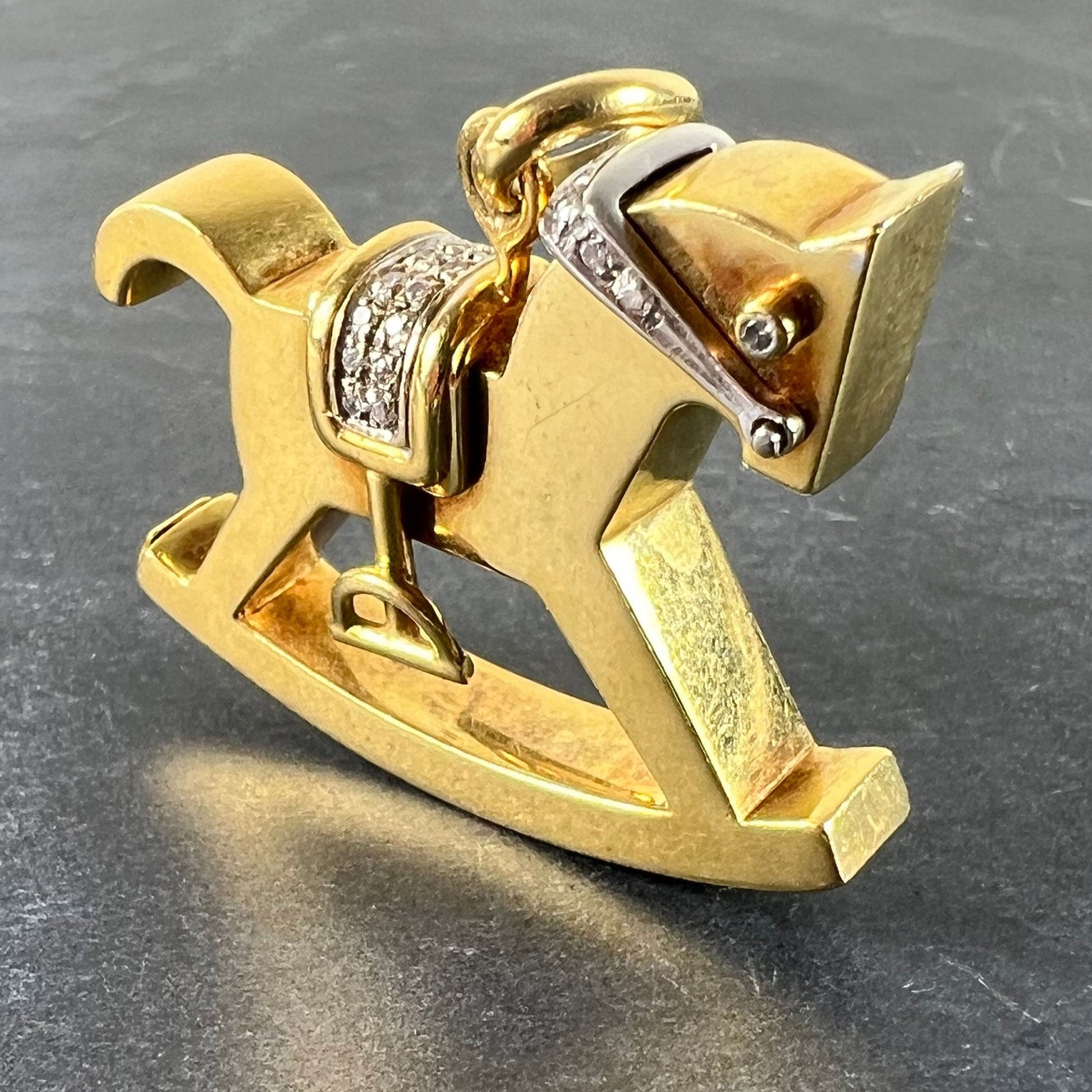 A yellow and white gold rockinghorse pendant with diamonds, on a grey background