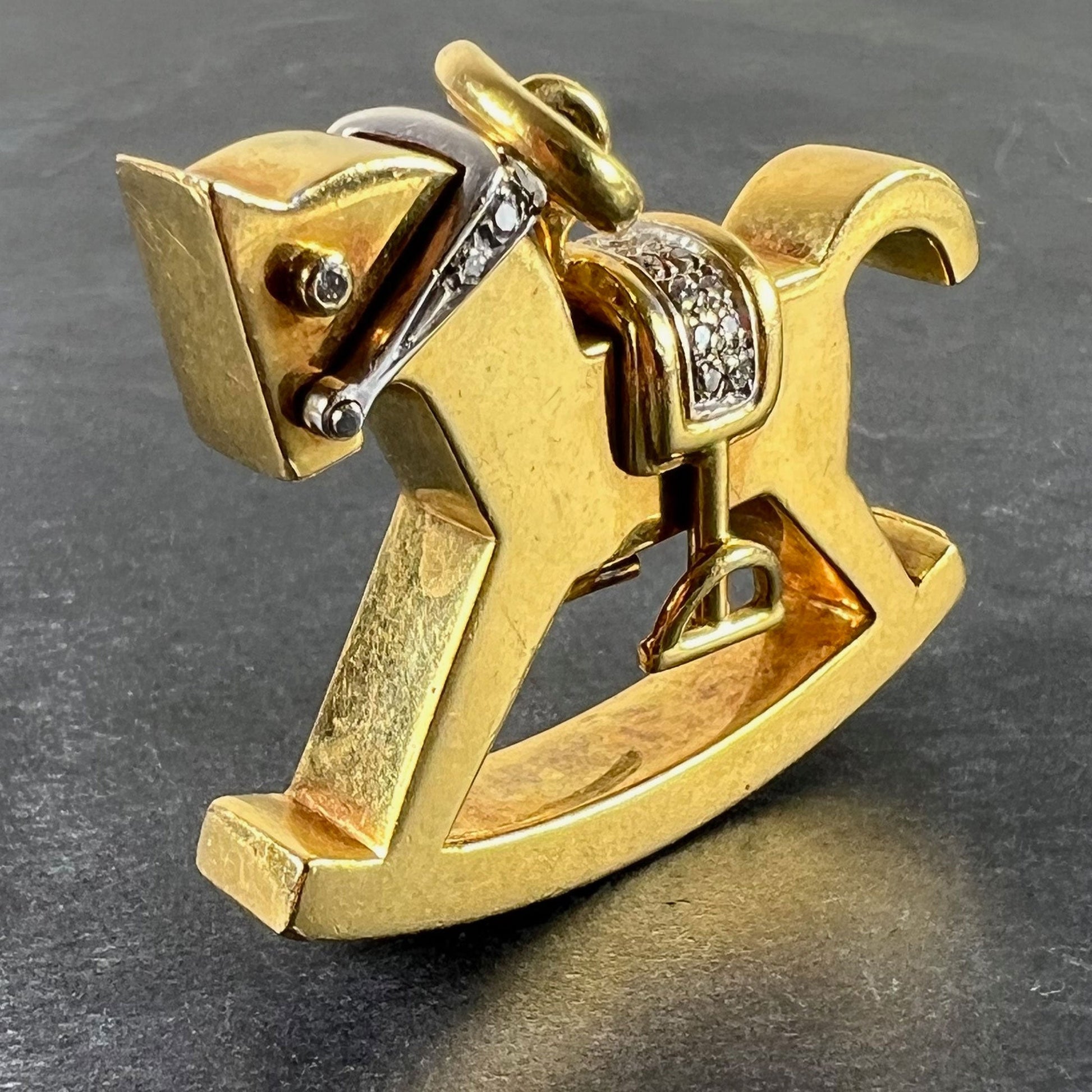 A yellow and white gold rockinghorse pendant with diamonds, on a grey background