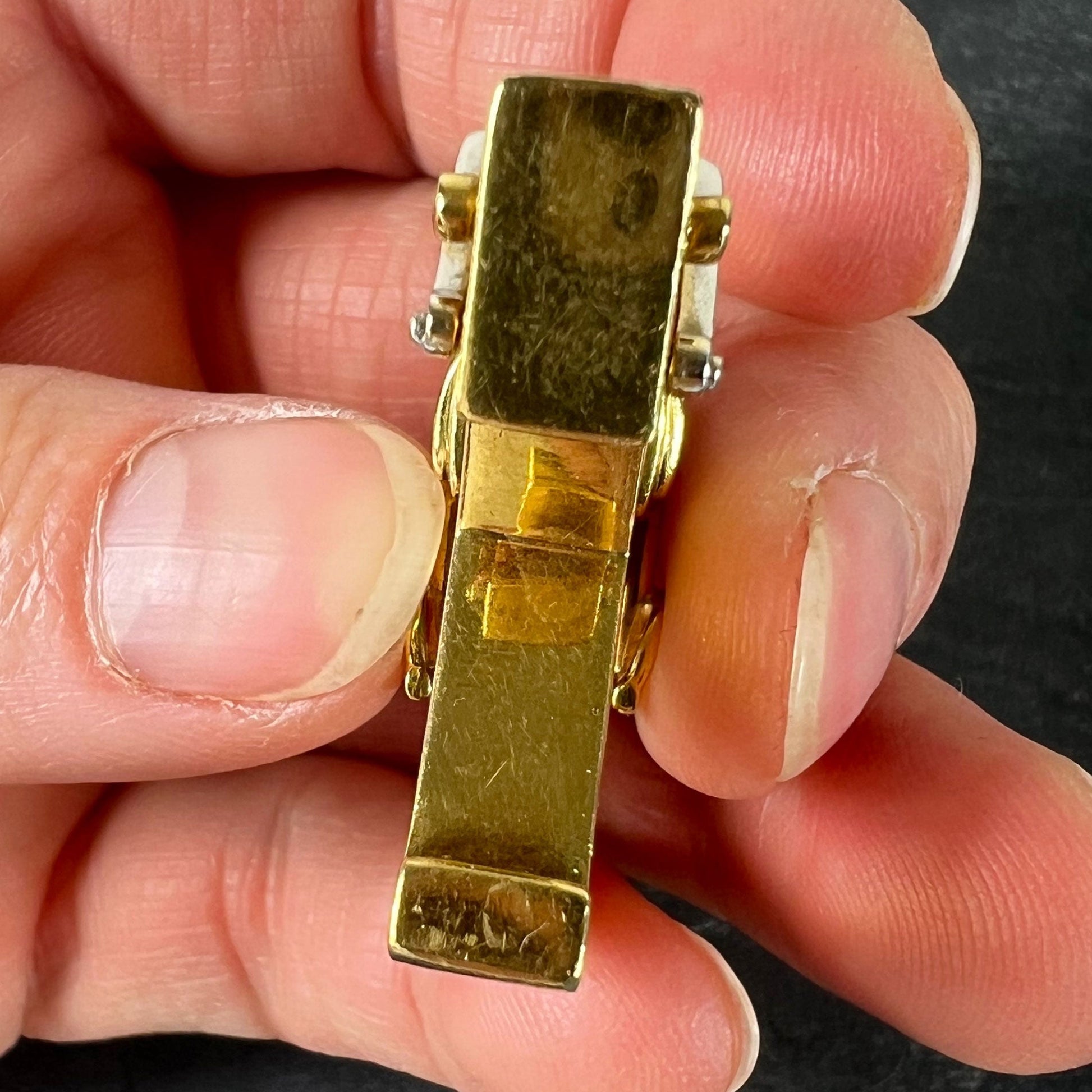 A yellow and white gold rockinghorse pendant with diamonds, held in a hand on a grey background