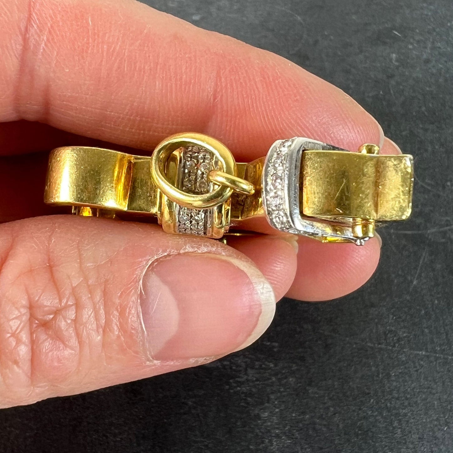 A yellow and white gold rockinghorse pendant with diamonds, held in a hand on a grey background