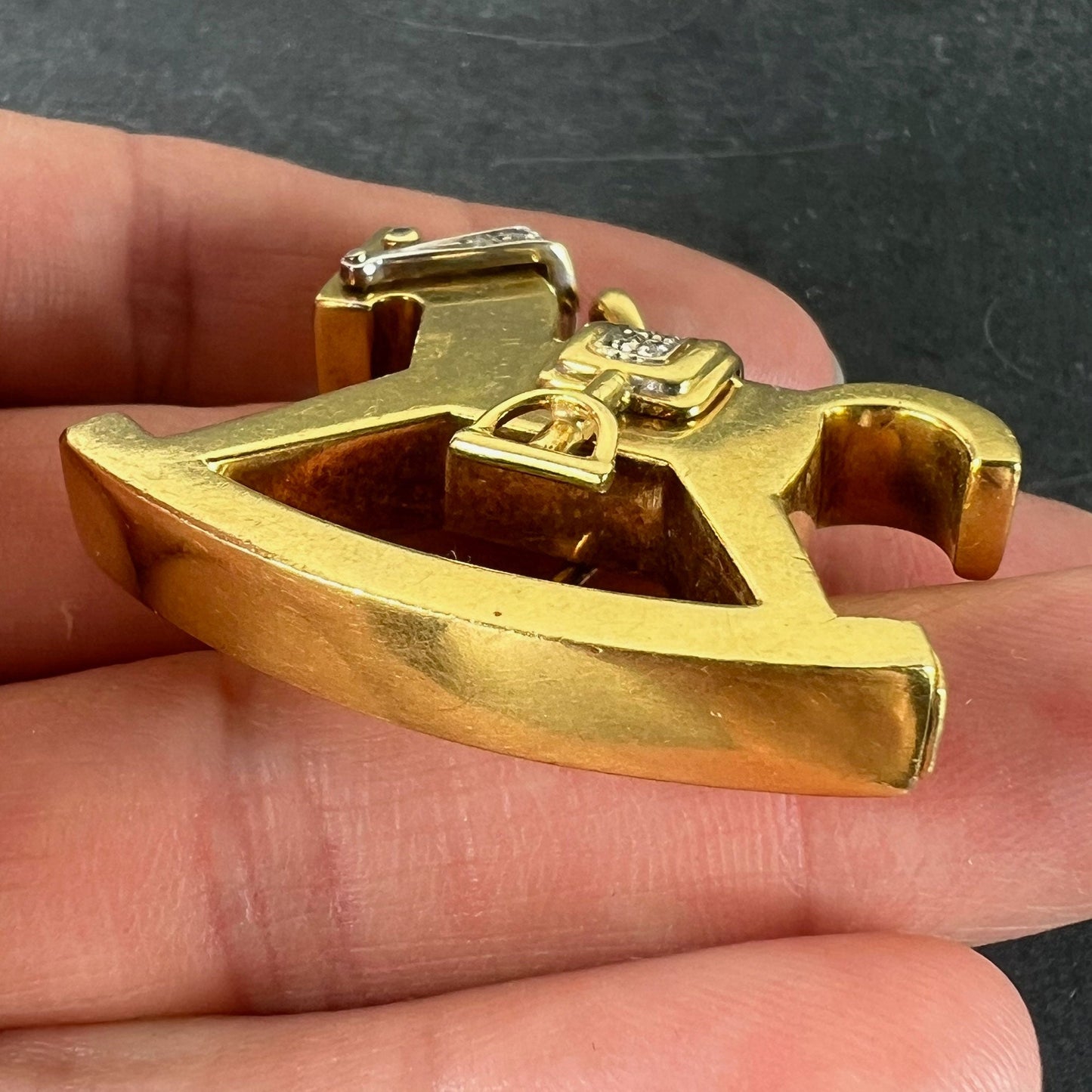 A yellow and white gold rockinghorse pendant with diamonds, held in a hand on a grey background