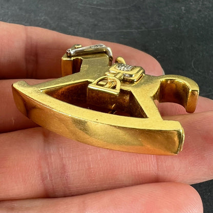 A yellow and white gold rockinghorse pendant with diamonds, held in a hand on a grey background
