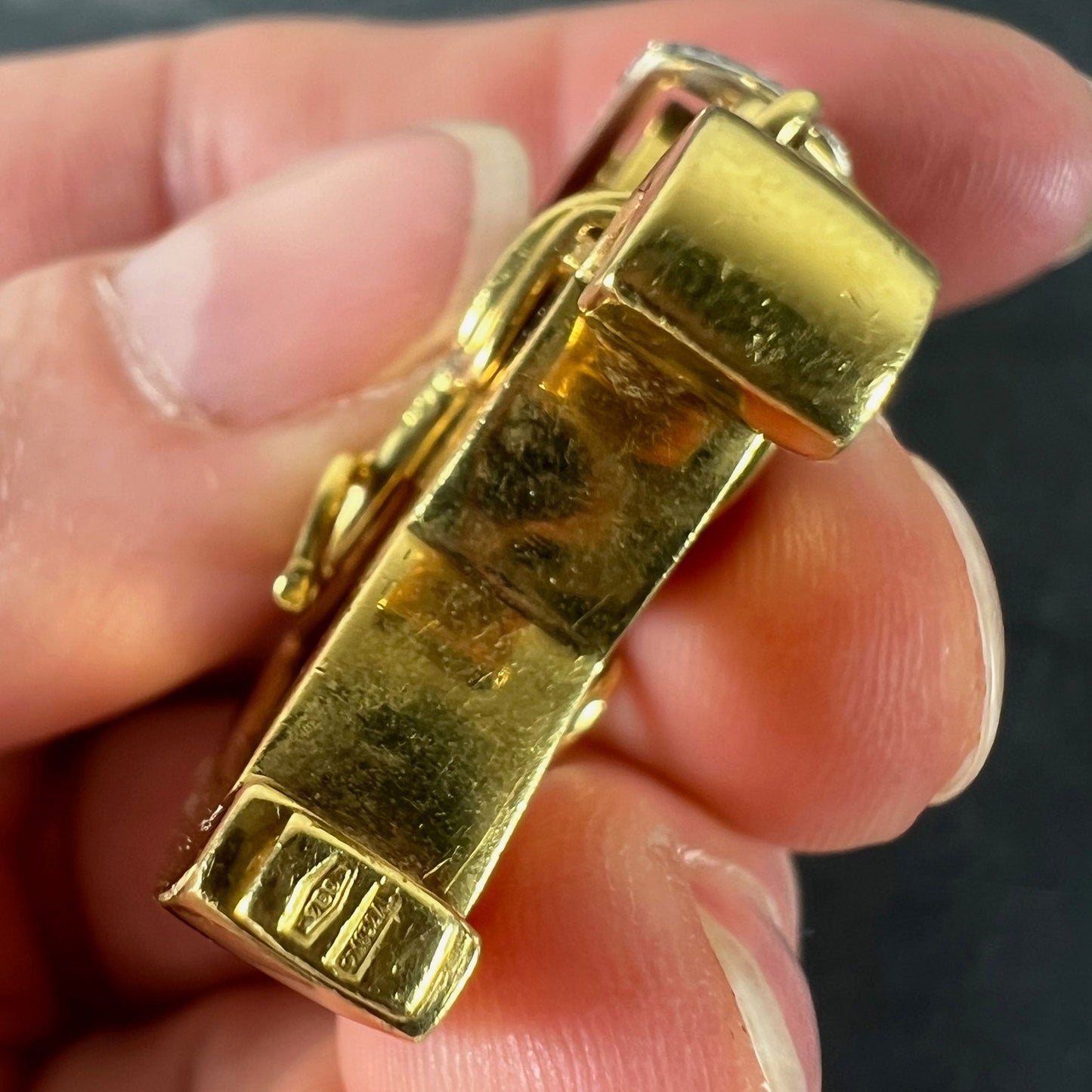 A yellow and white gold rockinghorse pendant with diamonds, held in a hand on a grey background