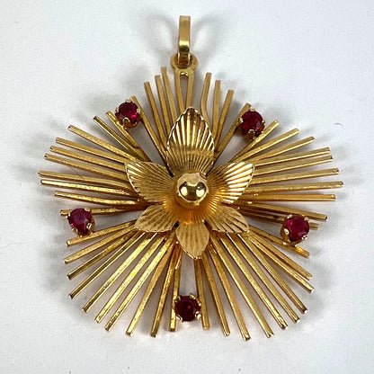 A yellow gold floral sunburst pendant with rubies, on a white background
